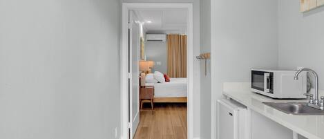 Habitación de hotel compacta con kitchenette, una cama y un baño visible a través de una puerta abierta.