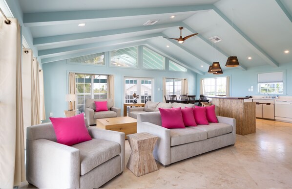 A spacious living room with light blue walls, large windows, and a kitchen area.