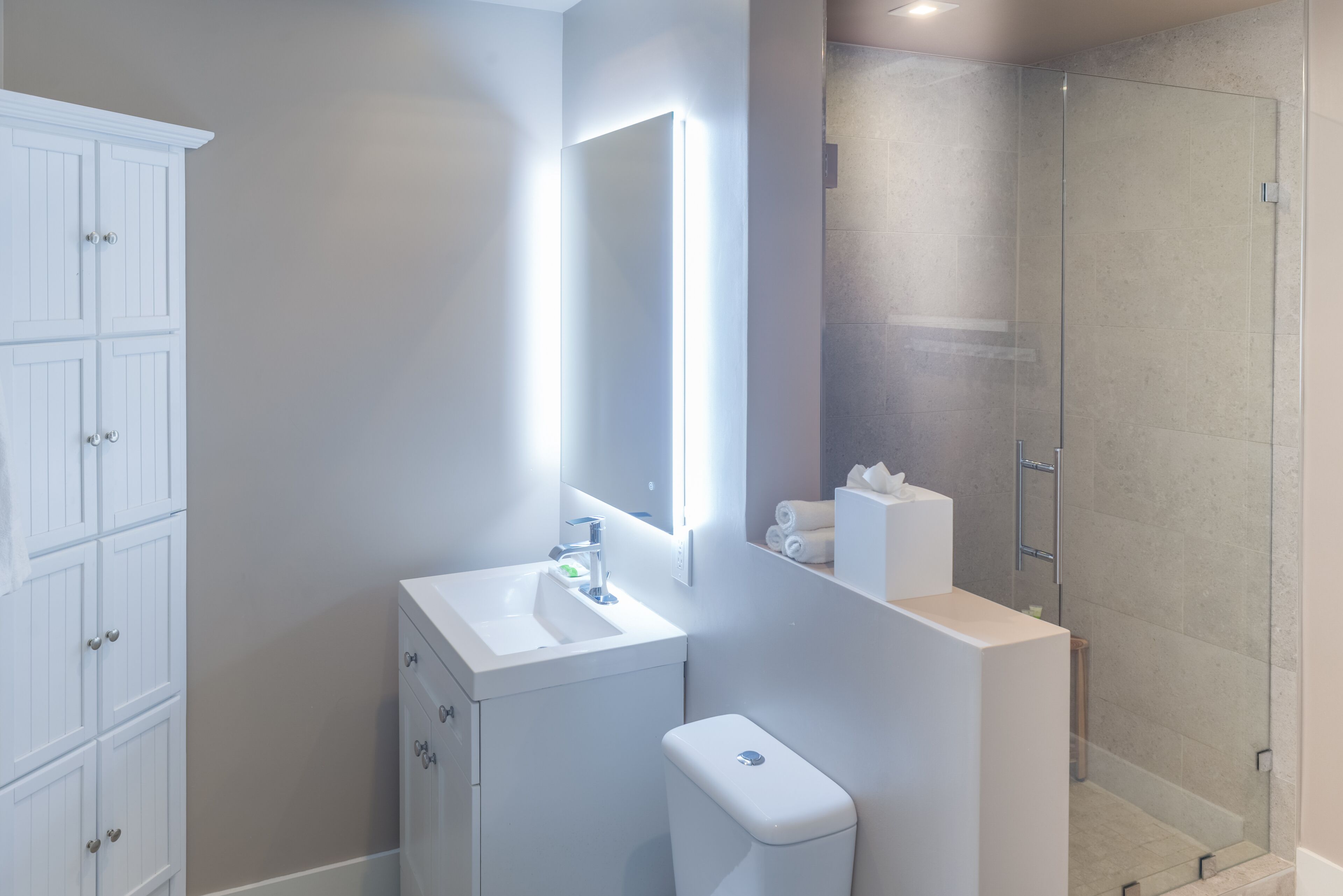 A modern bathroom with a white vanity, a glass shower enclosure, and a large mirror.