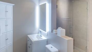 Un baño moderno con un tocador blanco, cabina de ducha con mampara de vidrio y un espejo grande.