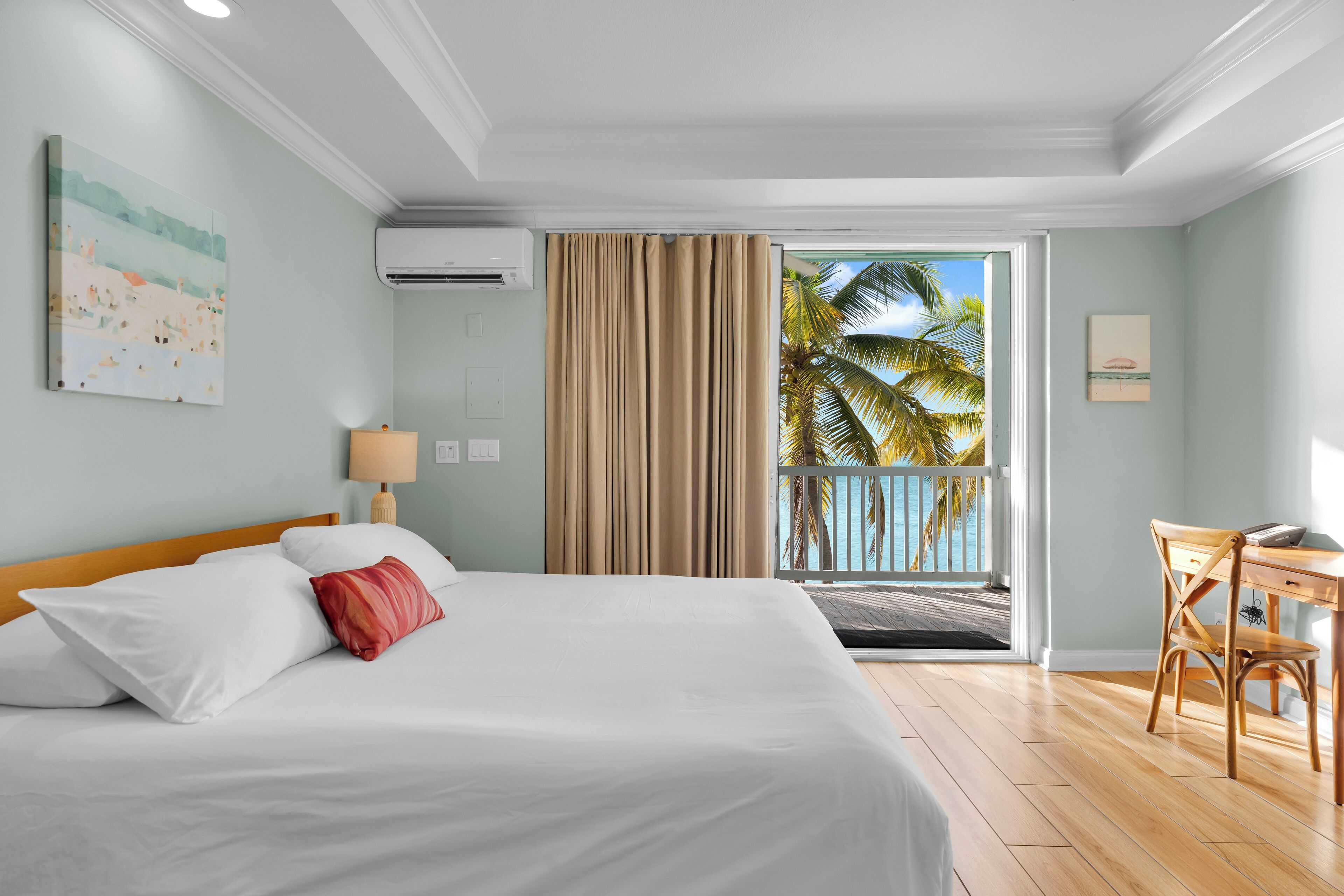 A hotel room with a bed, a desk, and a view of palm trees.