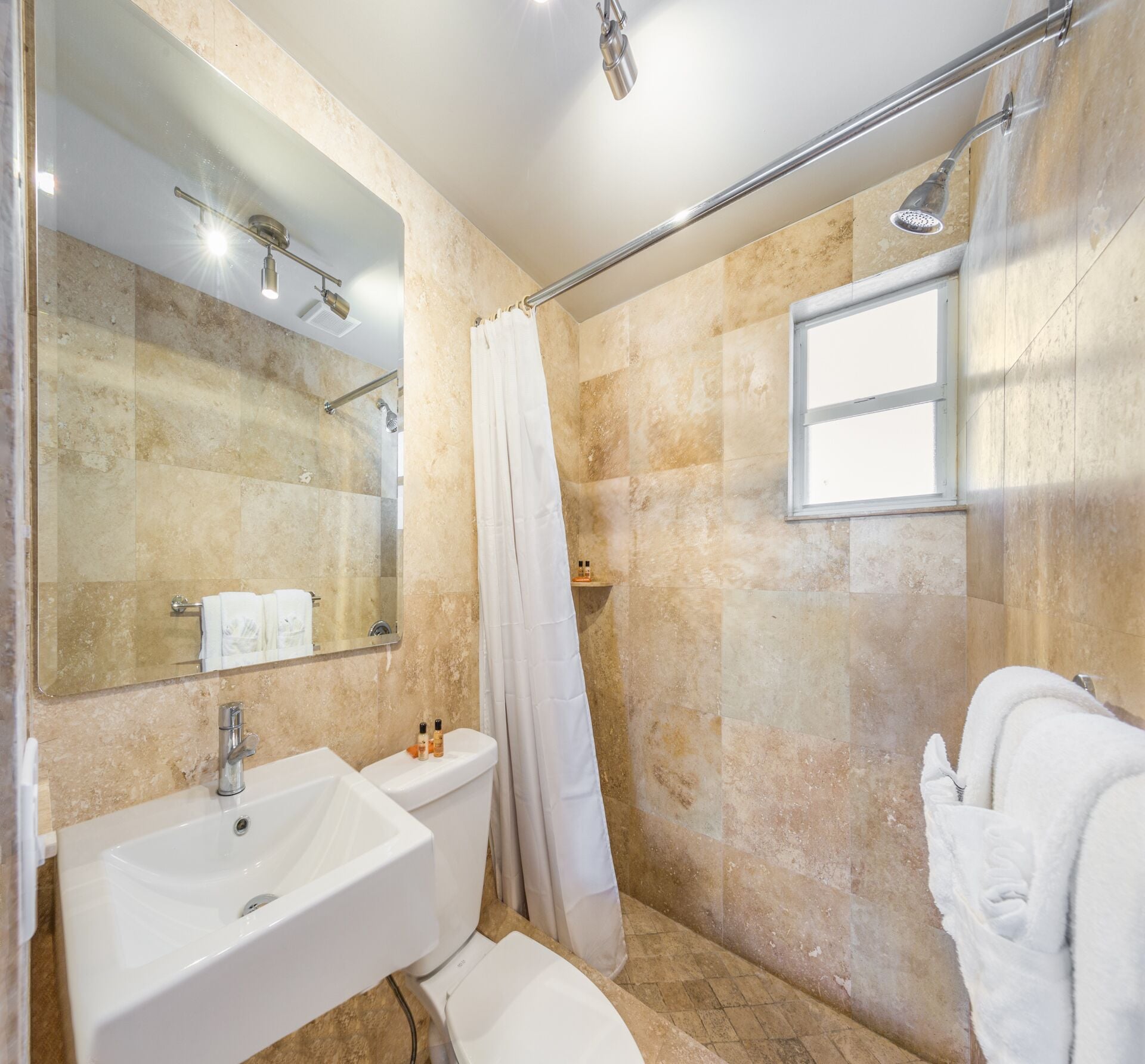 A bathroom with a shower, a sink, a toilet, and a mirror.