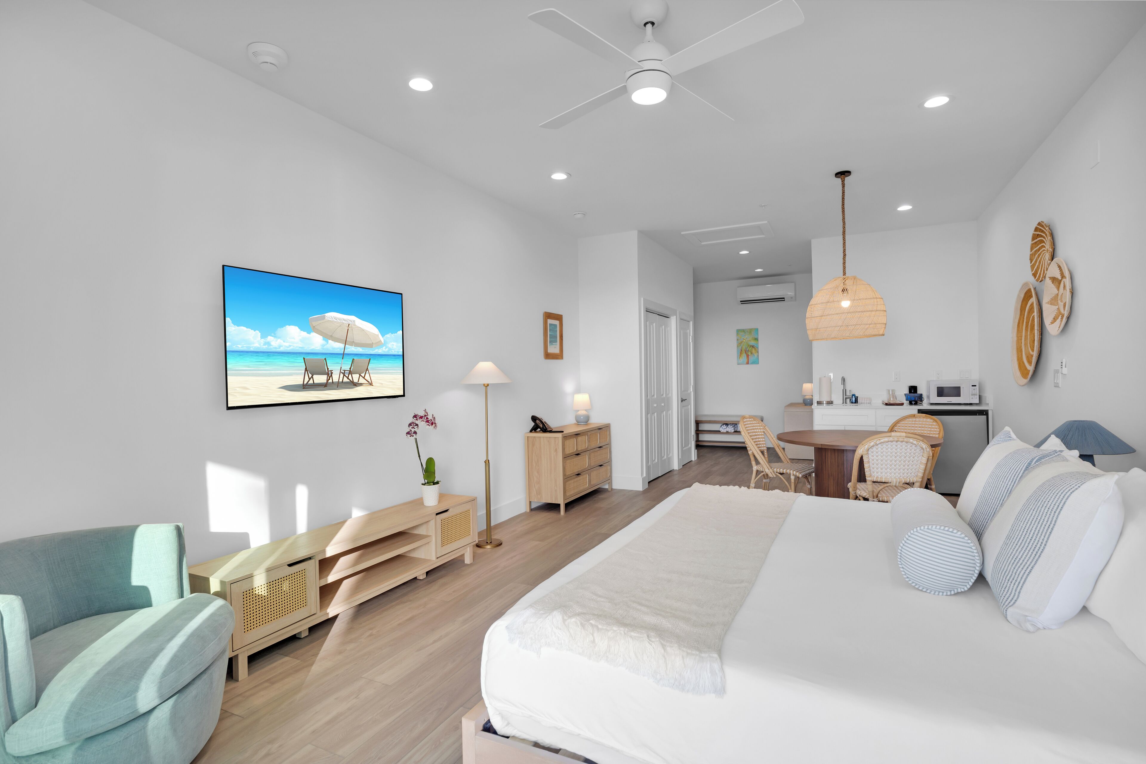 A modern bedroom with a large bed, a desk, and a chair. There is a painting of a beach scene on the wall.