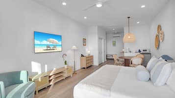 A modern bedroom with a large bed, a desk, and a chair. There is a painting of a beach scene on the wall.