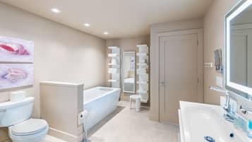 A modern bathroom with a toilet, sink, and bathtub. There are shelves with towels and a mirror above the sink.