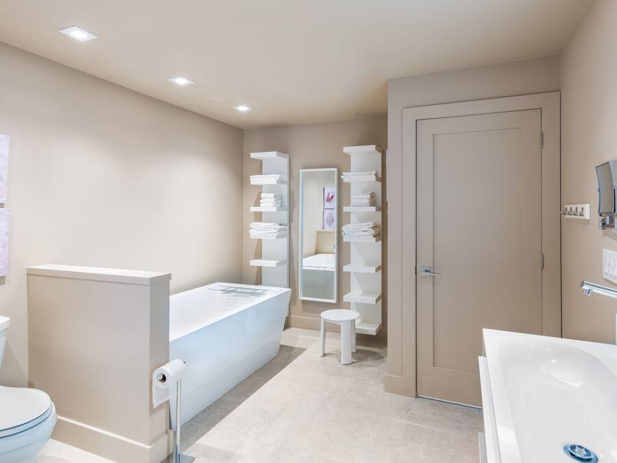 A modern bathroom with a toilet, sink, and bathtub. There are shelves with towels and a mirror above the sink.