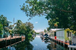 A canal with boats docked on both sides, surrounded by lush greenery and small houses.
