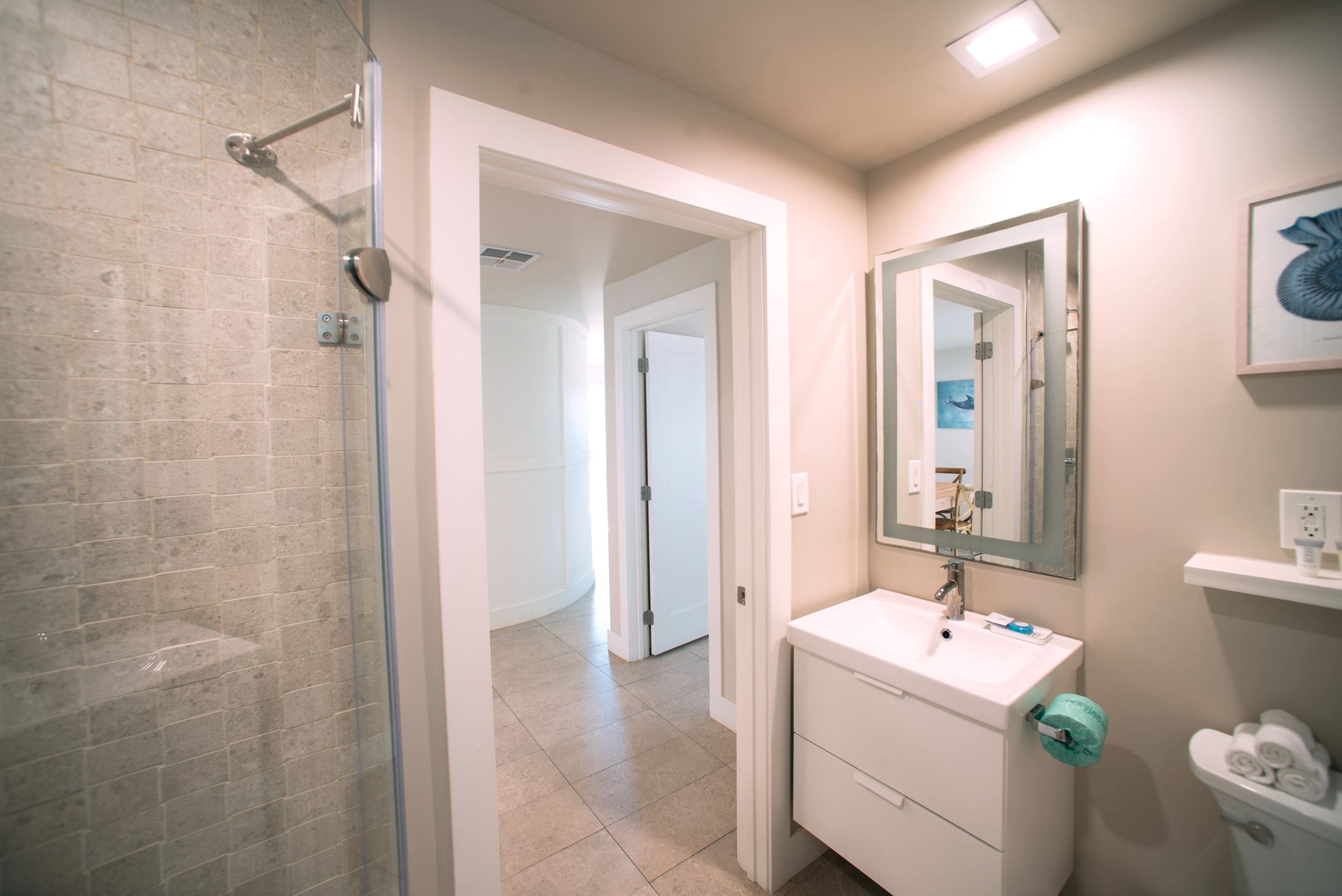 A bathroom with a glass shower enclosure, a white sink with a mirror above it, and a toilet with a towel holder.