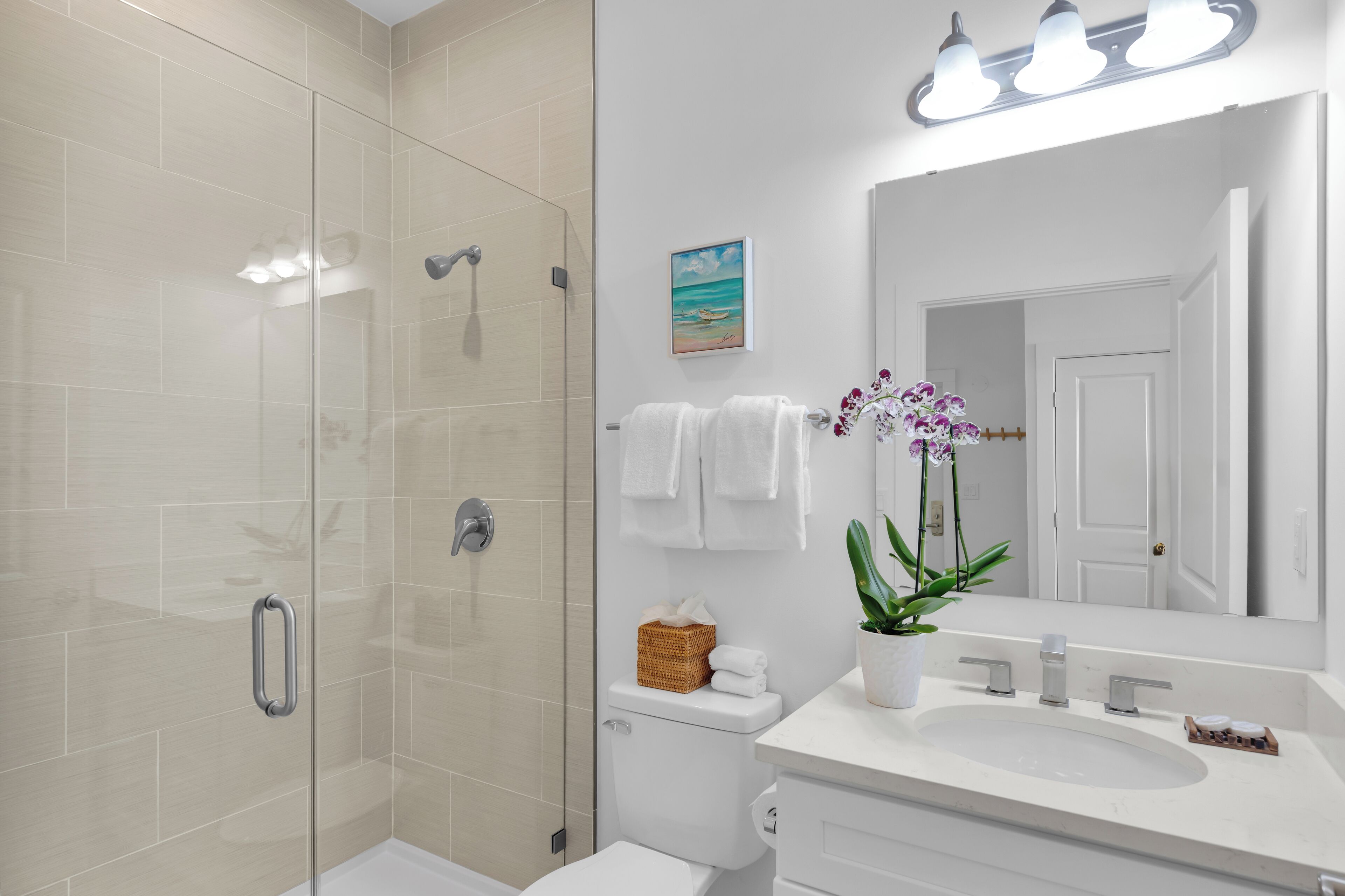 Un baño moderno con cabina de ducha de vidrio, un lavabo blanco y un espejo grande.