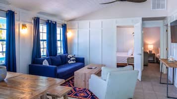 A room with a blue sofa, a wooden table, a striped armchair, and a bed in the background.