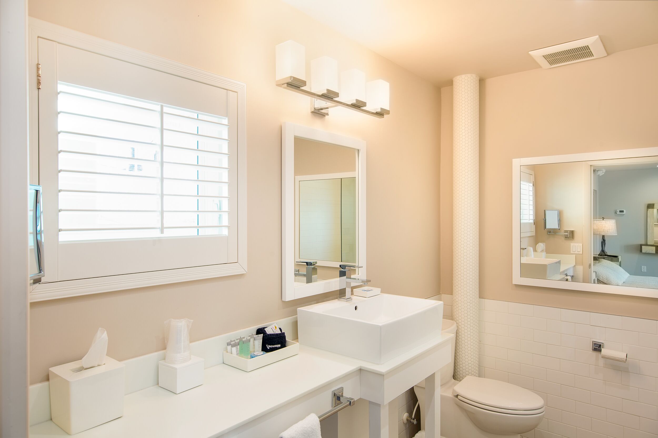 Une salle de bain avec une grande fenêtre, un lavabo, un miroir et des toilettes.