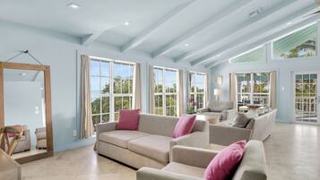 A spacious living area with large windows, a high ceiling, and a neutral color palette.