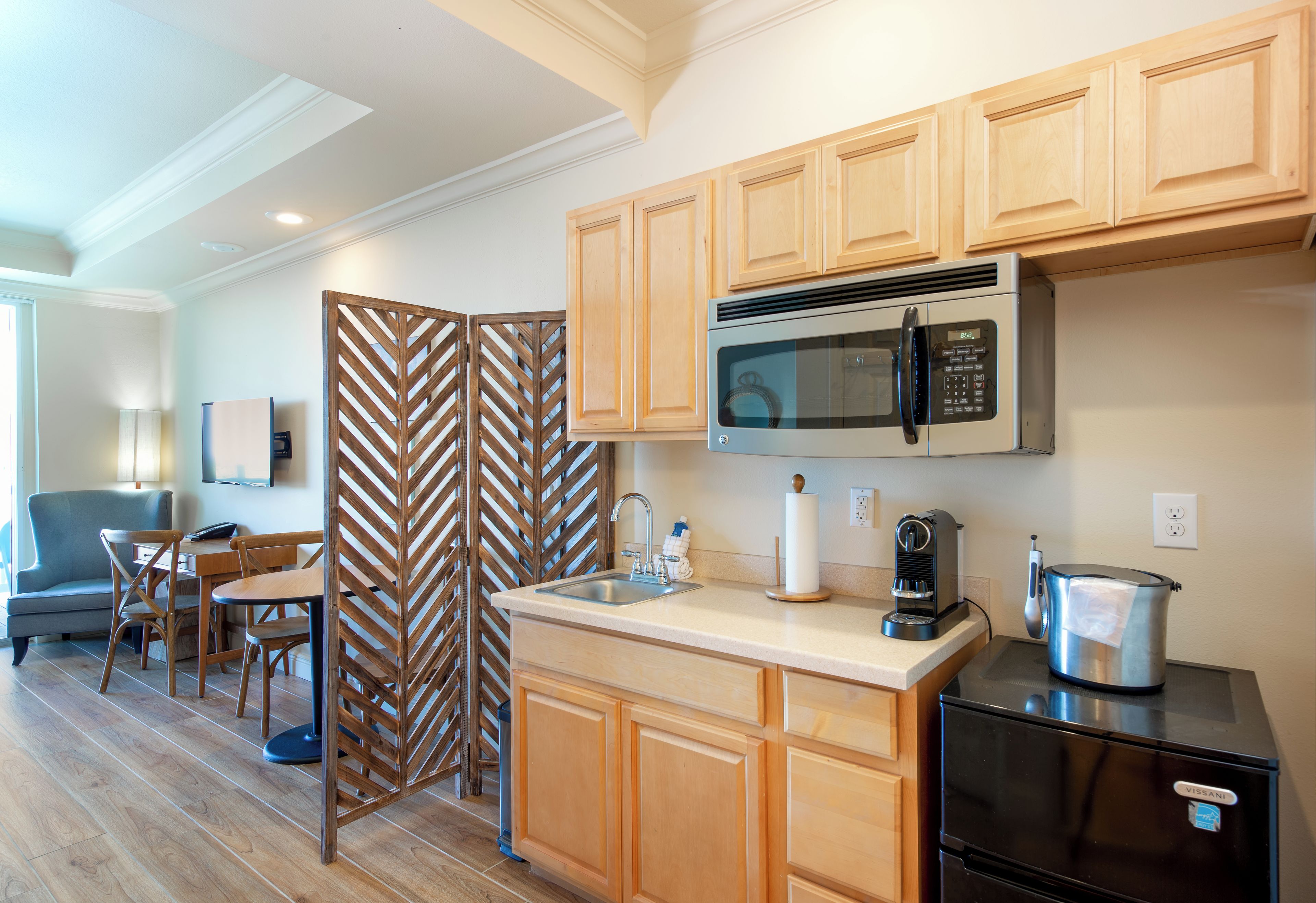 A compact kitchen with wooden cabinets, a built-in microwave, a coffee maker, and a kettle.