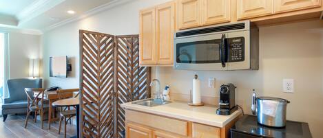 A compact kitchen with wooden cabinets, a built-in microwave, a coffee maker, and a kettle.