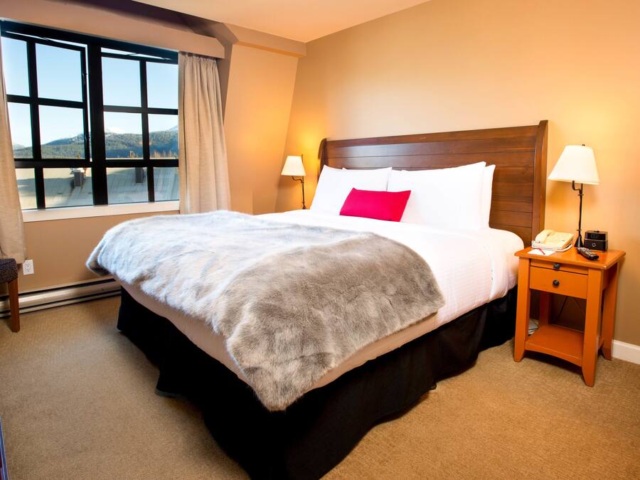A hotel room with a large bed, two bedside lamps, a nightstand with a telephone, and a window with curtains.