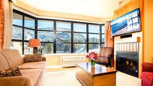 A cozy living room with a large window, a fireplace, and a television. - Sundial Hotel (Whistler)