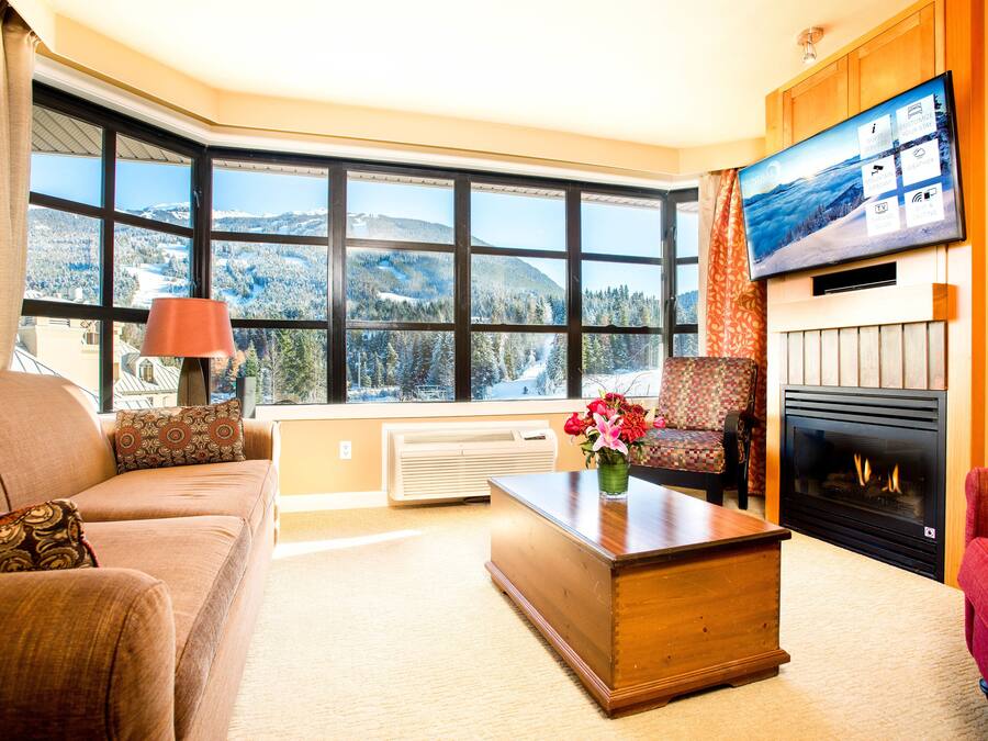 A cozy living room with a large window, a fireplace, and a television.