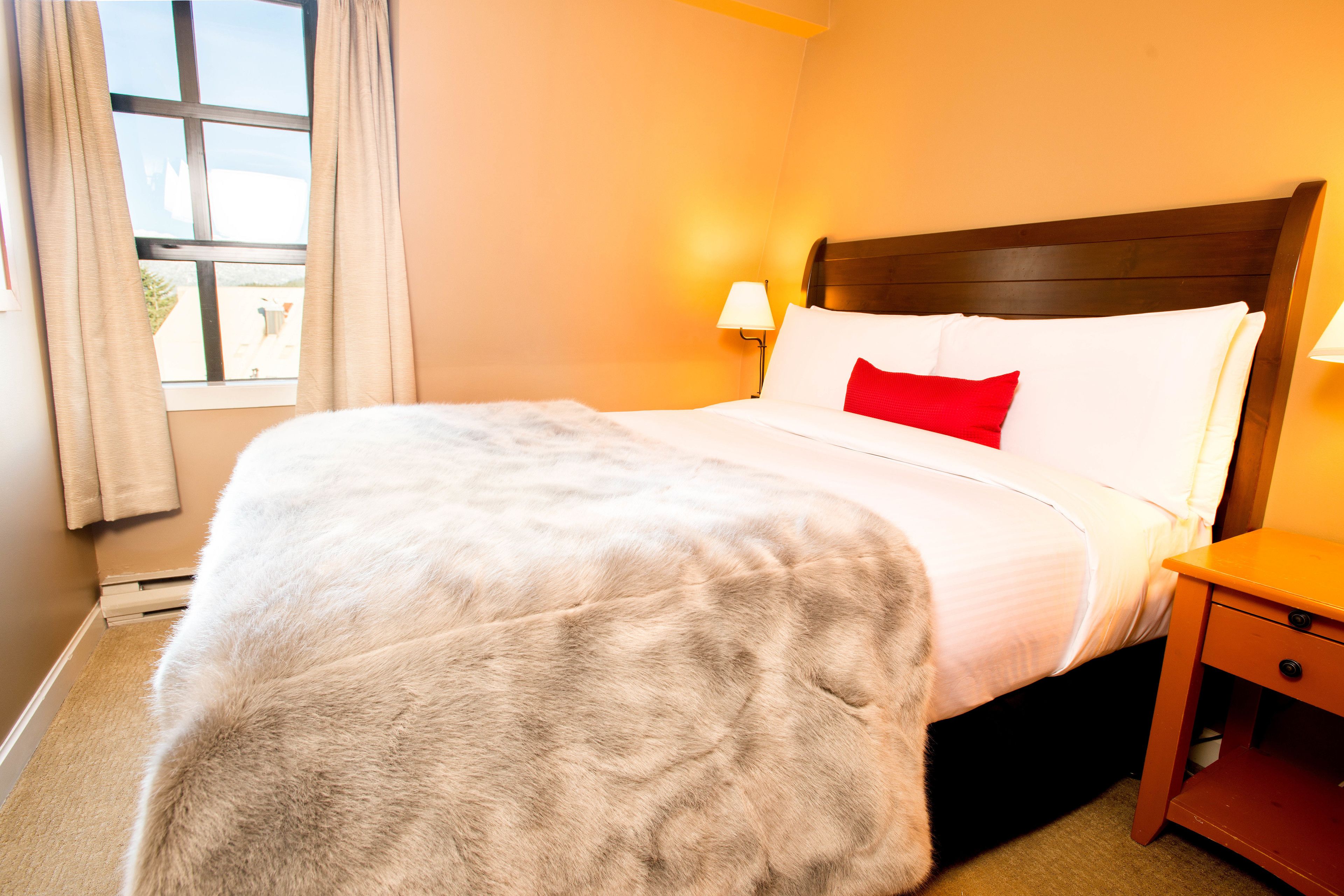 A neatly made bed with a white and red pillow, a wooden headboard, and a bedside table with a lamp.
