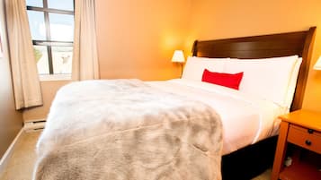 Un letto rifatto con cuscino bianco e rosso, una testiera in legno e un comodino con una lampada.