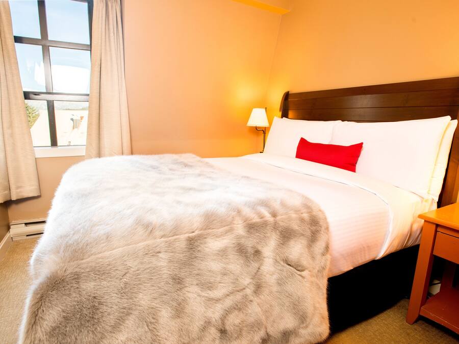 Un letto rifatto con cuscino bianco e rosso, una testiera in legno e un comodino con una lampada.