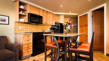 A kitchen with wooden cabinets, a black microwave, a granite countertop, and a bar stool with a vase of flowers.