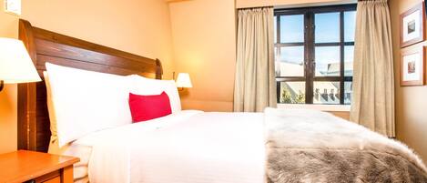 A hotel room with a large bed, two bedside tables, a window with curtains, and a view of buildings outside.