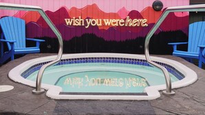 A hot tub with a mountain backdrop, two blue Adirondack chairs, and a mural with the text 'wish you were here.' - Sundial Hotel (Whistler)