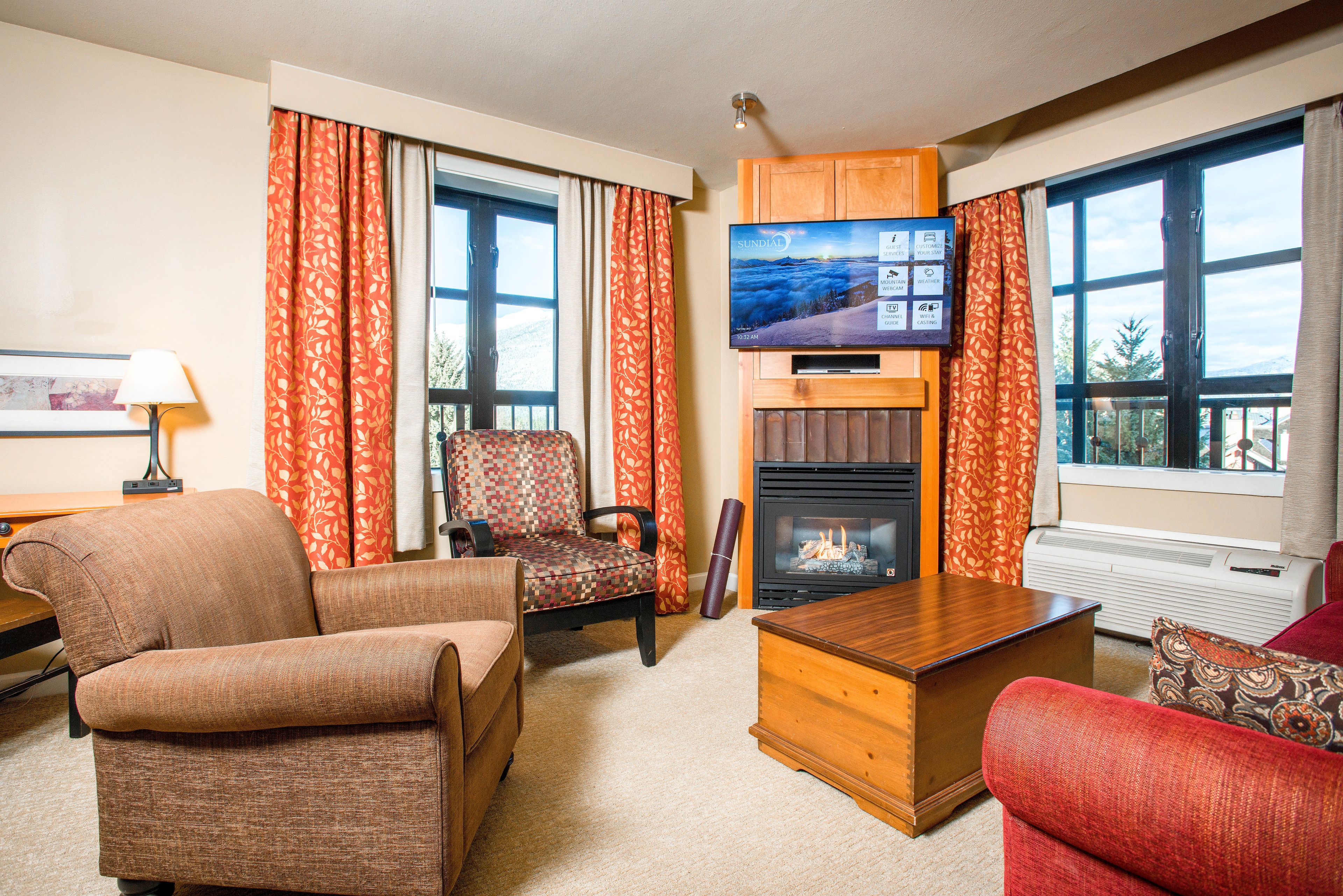 A living room with a fireplace, a television, and large windows with curtains.