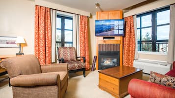 A living room with a fireplace, a television, and large windows with curtains.