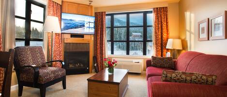 A cozy living room with a fireplace, a television, and a large window with curtains.