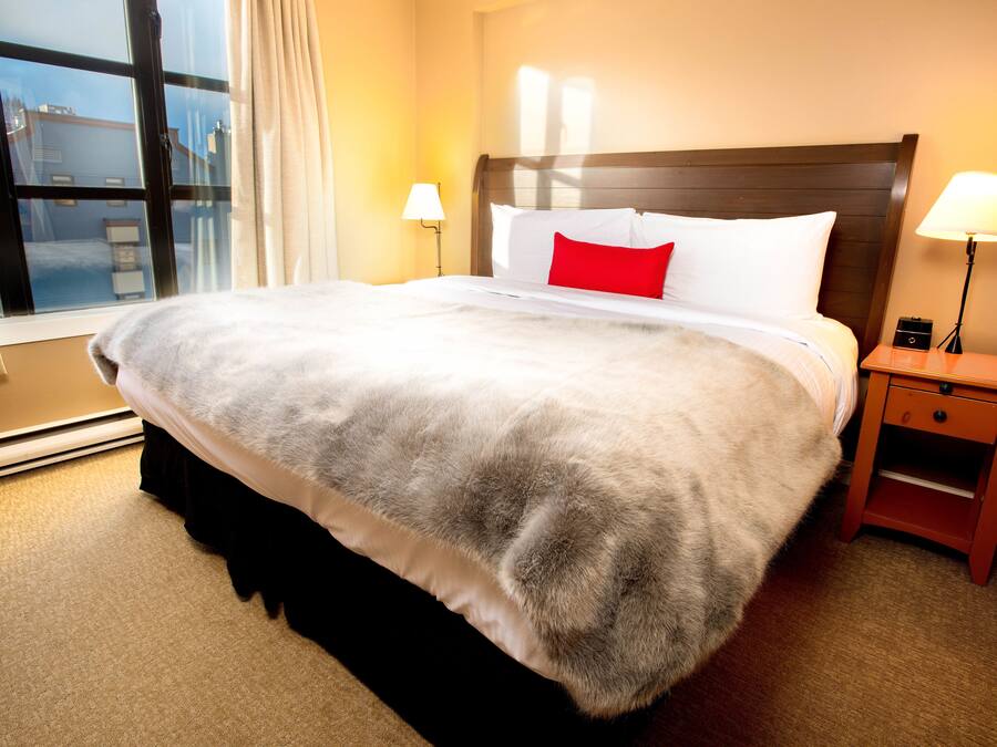 A hotel room with a large bed, a nightstand, a lamp, and a window with curtains.