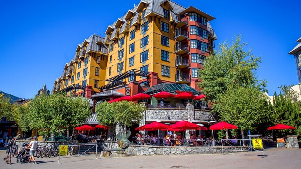 A multi-story hotel with outdoor seating and red umbrellas. - Sundial Hotel (Whistler)