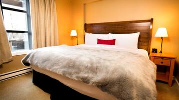 A hotel room with a large bed, two bedside lamps, a wooden headboard, and a window with curtains.