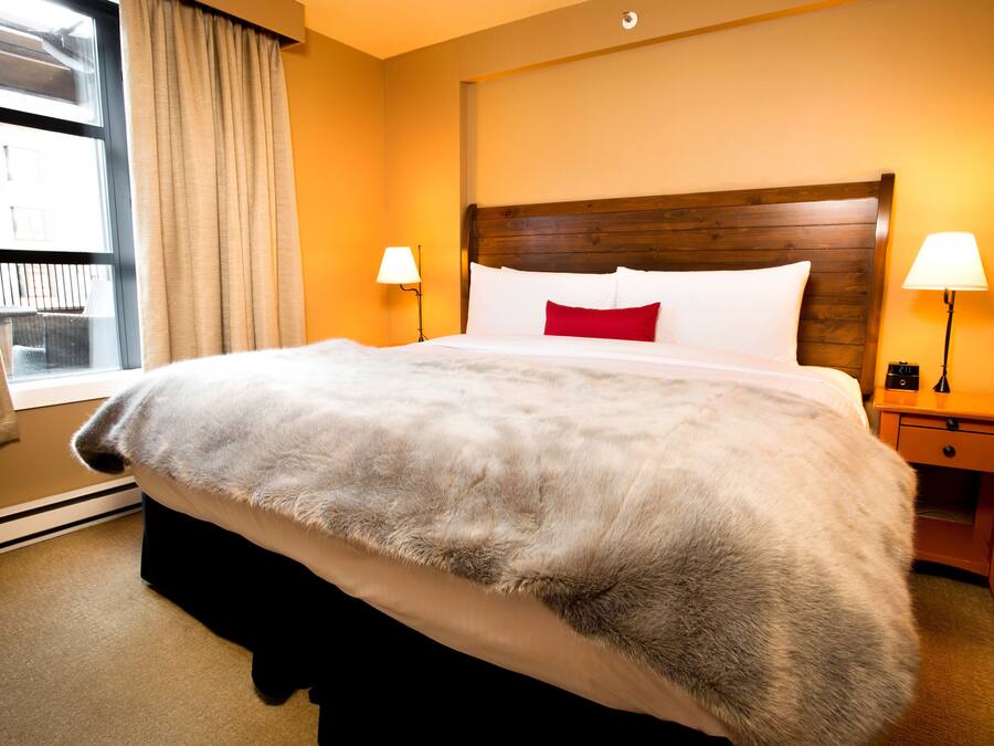 A hotel room with a large bed, two bedside lamps, a wooden headboard, and a window with curtains.