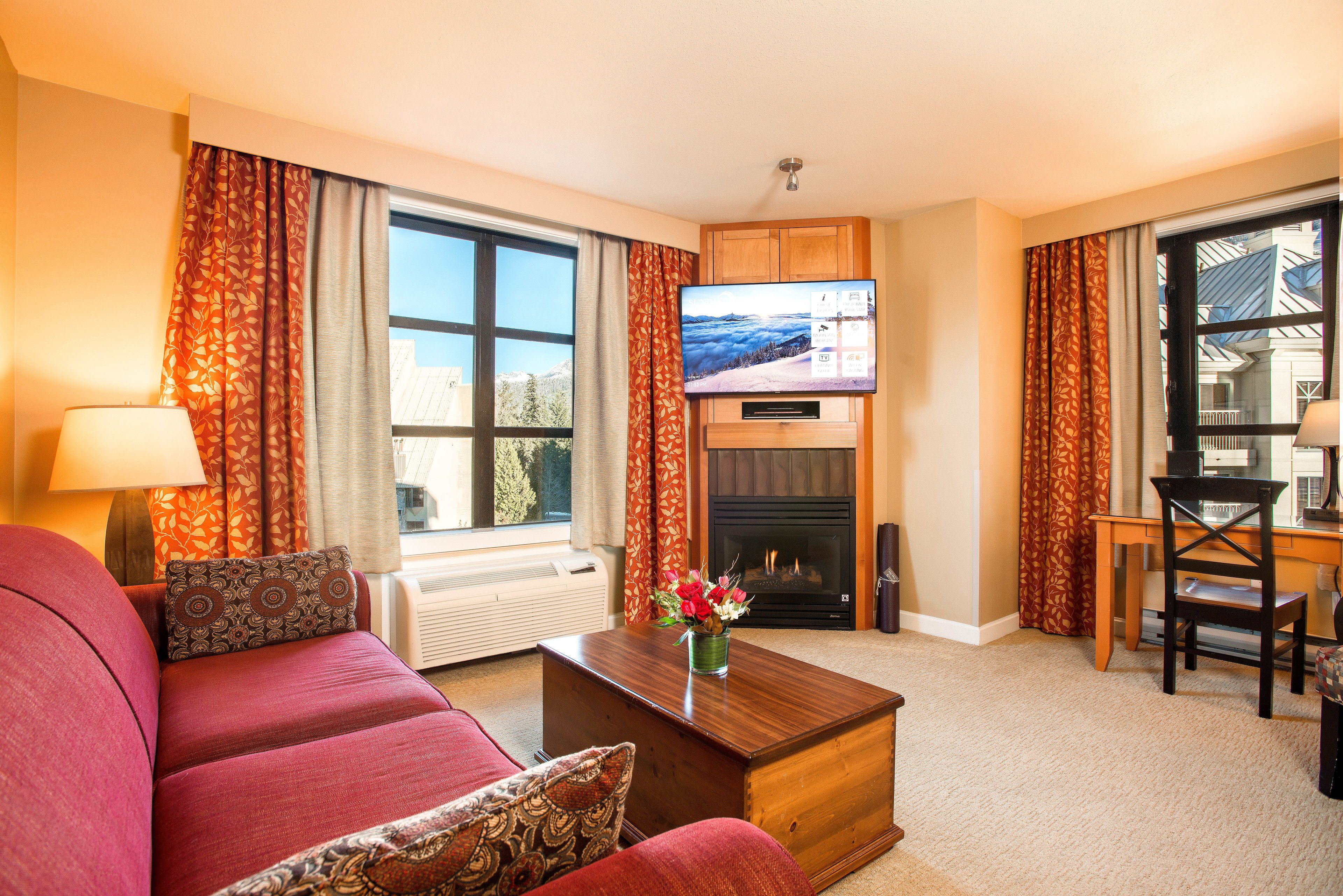 A living room with a sofa, a coffee table, a fireplace, a television, and a view of the outdoors.