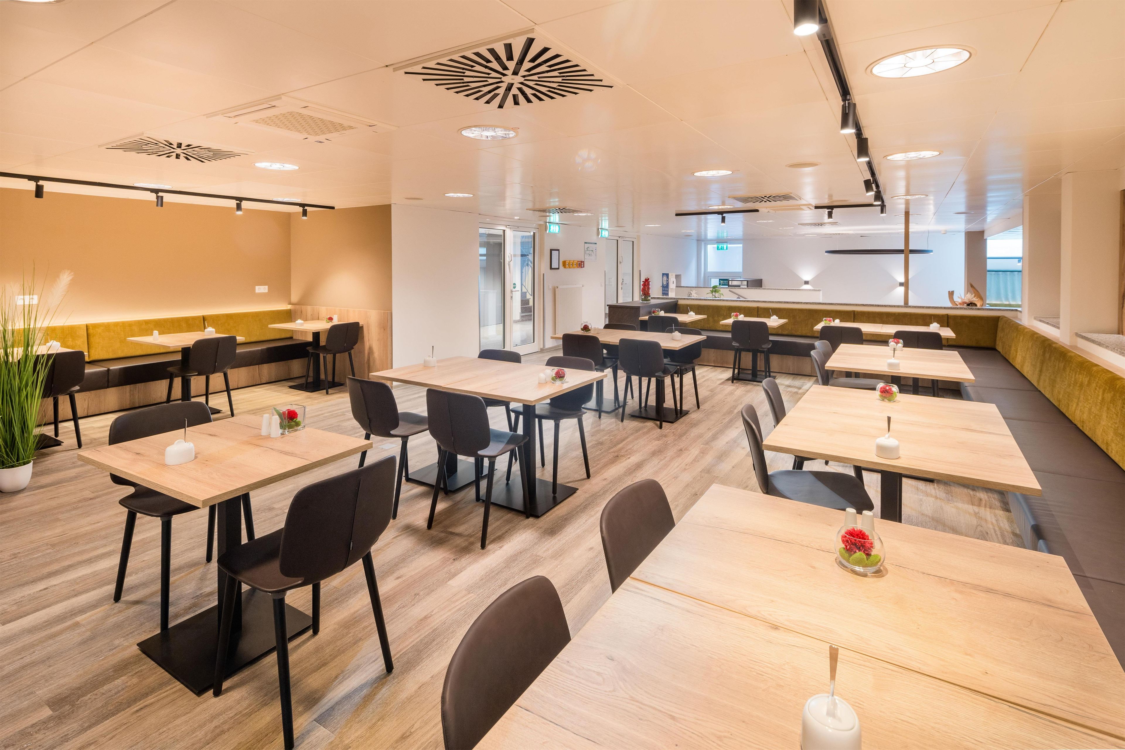 A modern dining area with multiple tables and chairs, a reception desk, and a view of the outside.