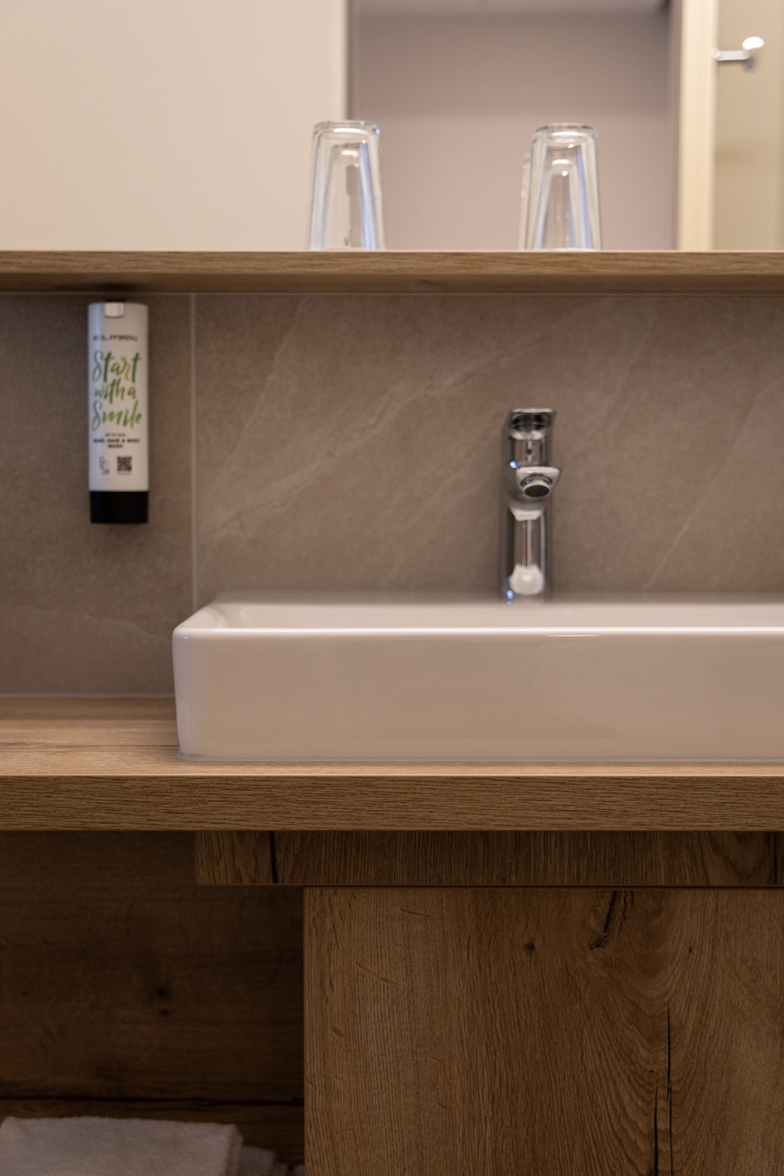A bathroom with a wooden vanity, a white sink, and a mirror.