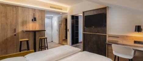 Ein modernes Hotelzimmer mit einem Bett, einem Schreibtisch mit Stuhl, einem Fernseher und einem Kleiderschrank.