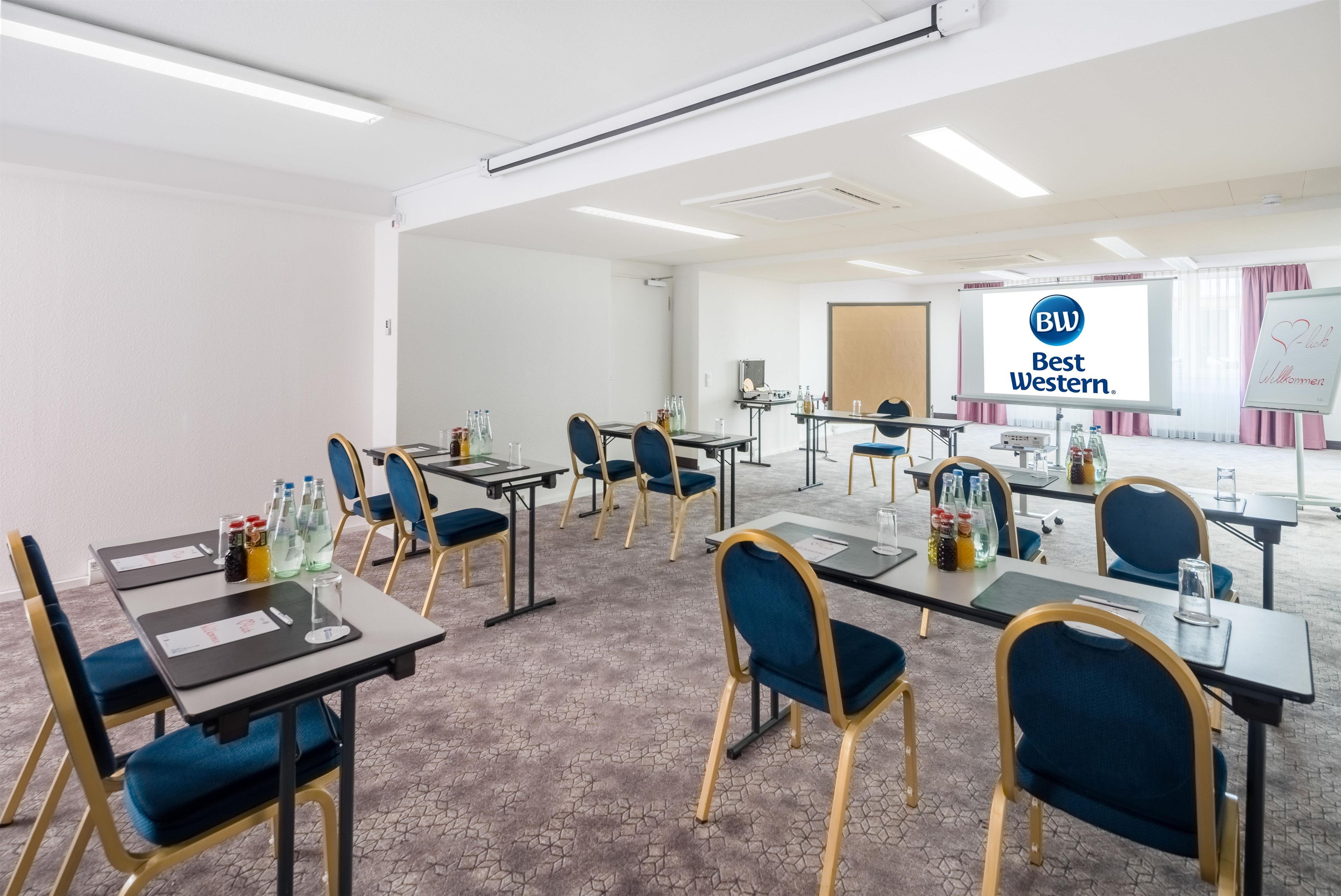 A conference room with tables, chairs, and a presentation screen displaying 'BW Best Western.'