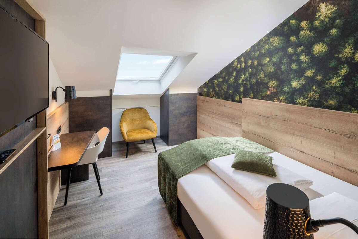 Een kleine kamer met een bed, bureau, stoel en dakraam.