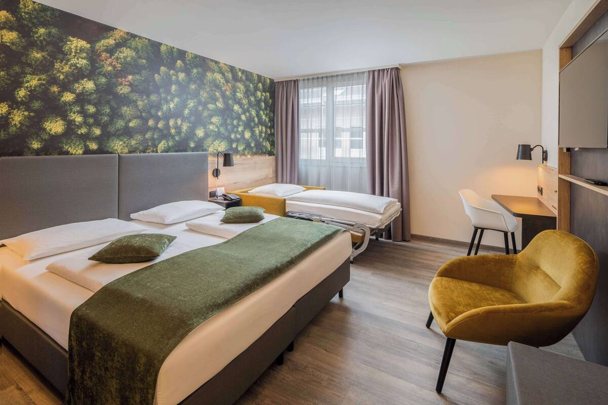Een hotelkamer met twee bedden, een bureau, een stoel en een groot raam met gordijnen.