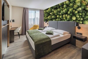 Habitación de hotel moderna con cama, escritorio, silla, televisor y un elemento decorativo en la pared verde.