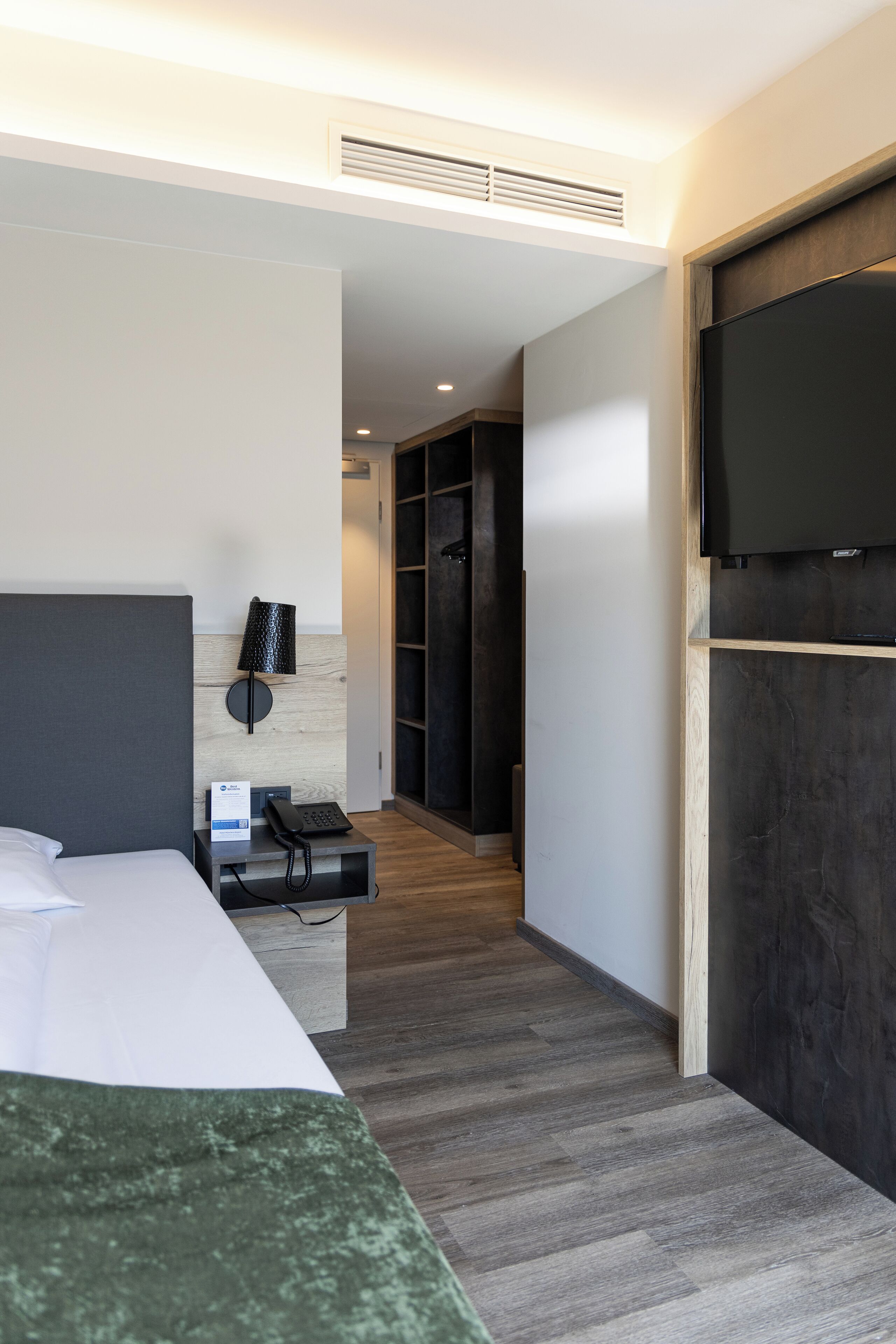 A hotel room with a bed, a bedside table with a lamp, a phone, and a TV mounted on the wall.