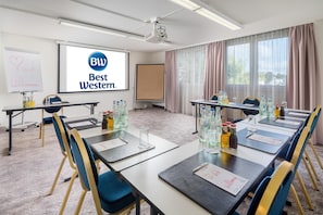 A conference room with a projector screen displaying 'BW Best Western' logo, tables with water bottles, and a whiteboard with a heart drawing and text.