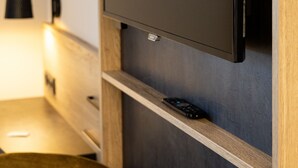 Une chambre moderne équipée d’un téléviseur à écran plat fixé au mur, d’une étagère en bois située en dessous et d’une télécommande posée sur l’étagère.