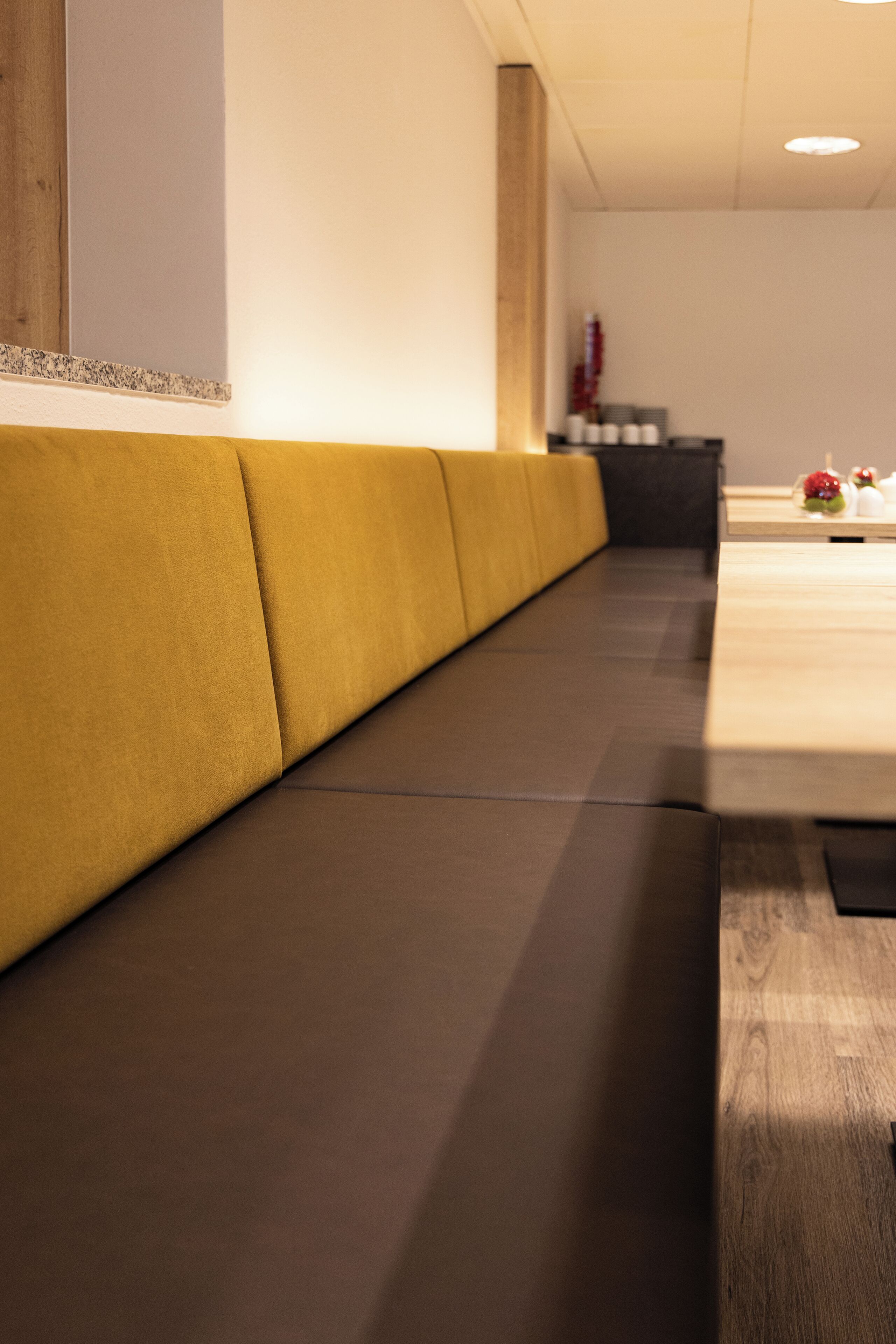 A modern hotel lobby with a long, cushioned bench along the wall, a reception desk, and a wooden floor.