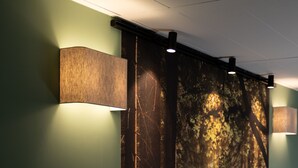 Un couloir orné d’une grande fresque représentant une scène de forêt, d’un luminaire fixé au mur et d’un panneau mural texturé.
