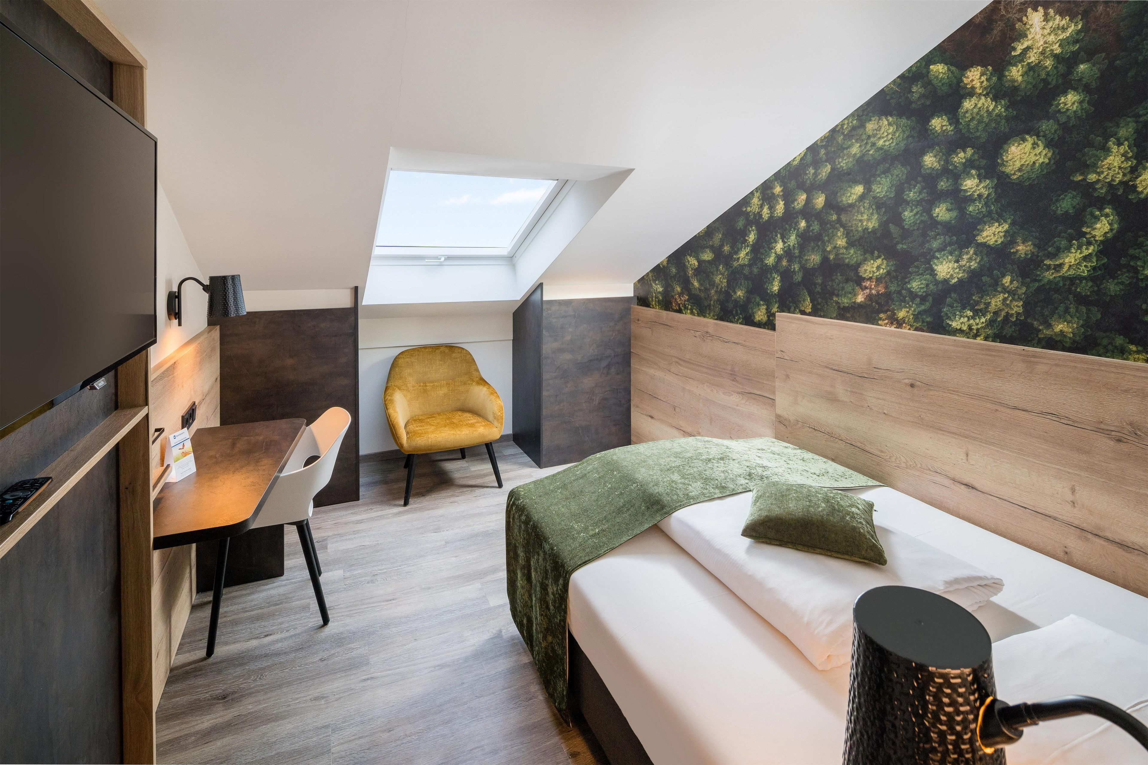 Una habitación compacta con tragaluz, una cama, un escritorio, una silla y una pared con diseño de hojas.