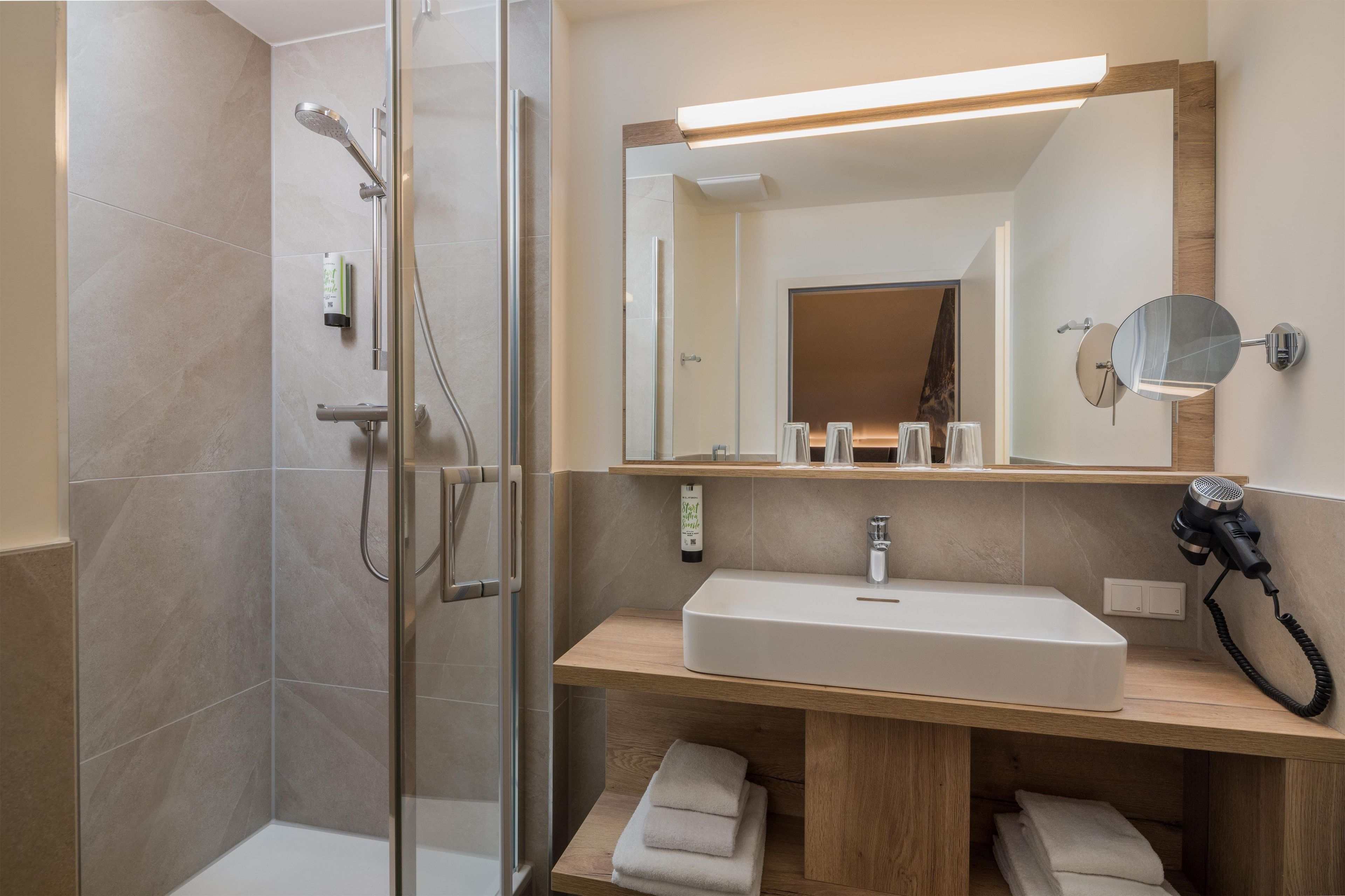 A modern bathroom with a glass shower enclosure, a wooden vanity with a sink, and a hairdryer.