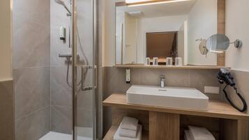 A modern bathroom with a glass shower enclosure, a wooden vanity with a sink, and a hairdryer.